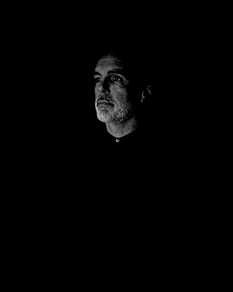 Man with a contemplative expression in a dark, minimalistic portrait symbolizing structure, order, and inner mastery
